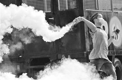 12月2日，泰國曼谷，一名反政府示威者在總理府附近向負責執(zhí)勤的警察投擲催淚彈。英拉請求示威者不要再試圖占領(lǐng)政府工作部門，不要逼迫政府工作人員選邊站。