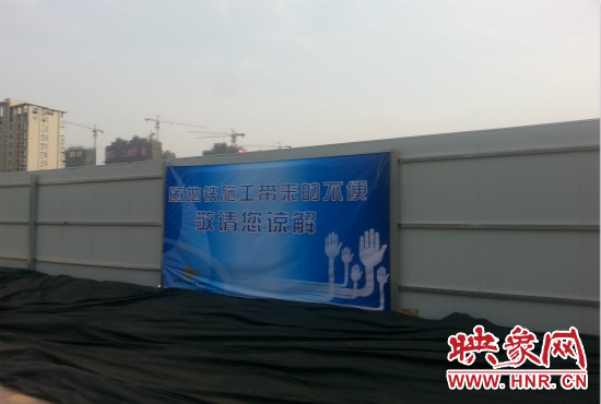 道路南側(cè)圍起了白色的圍擋，墻上標(biāo)示著“因地鐵施工帶來的不便敬請您諒解”的提示牌。