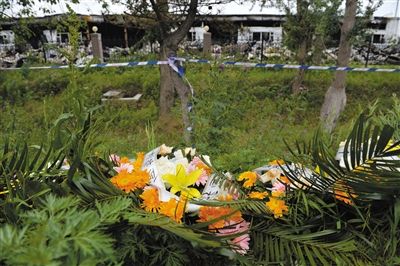 昨日，吉林省德惠市吉林寶源豐禽業(yè)有限公司燃燒事故現(xiàn)場警戒線外，遇難者家屬在路邊擺放了花圈祭奠逝去的親人。吳江 攝