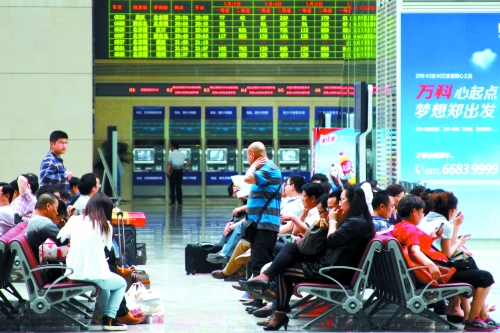 候車大廳溫度很高，一名乘客一手扇風(fēng)、一手擦汗