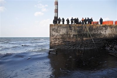 昨日，山東青島，清污人員正在海邊清理油污。