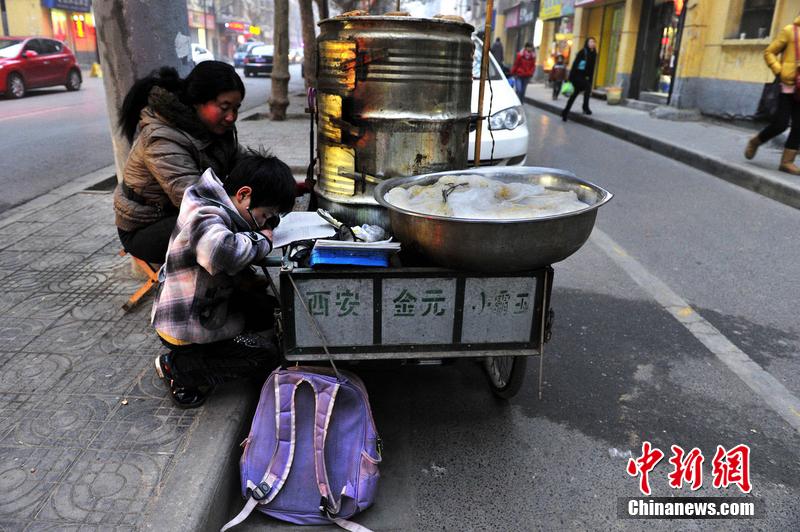 男孩西安路燈下寫(xiě)作業(yè) 媽媽邊賣(mài)紅薯邊輔導(dǎo)