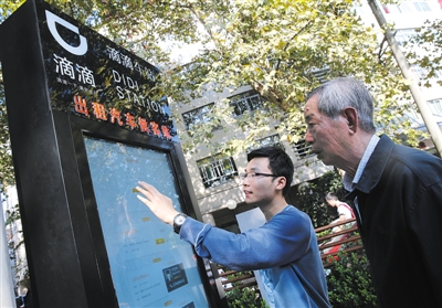 10月15日，滴滴工作人員（左）指導(dǎo)乘客使用“滴滴車站”的電子屏預(yù)約出租車。