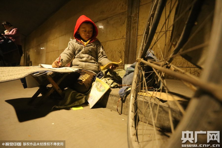2015年11月8日晚，鄭州，7歲男孩涵洞橋下陪父母練攤，路邊燈下坐小馬扎上寫(xiě)作業(yè)。