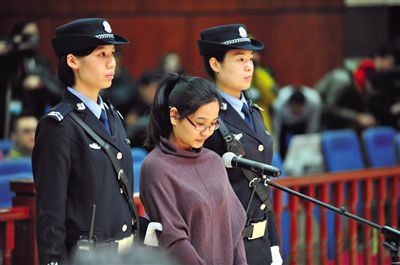 被告人盧梅低著頭，站在朝陽法院刑事審判庭的被告席上。