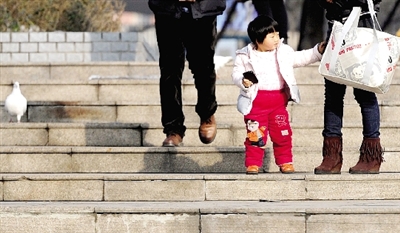 昨天中午，一女孩拉著家長(zhǎng)的手在紫荊山公園曬太陽(yáng)，氣溫升高，孩子的棉衣解開(kāi)了扣子。